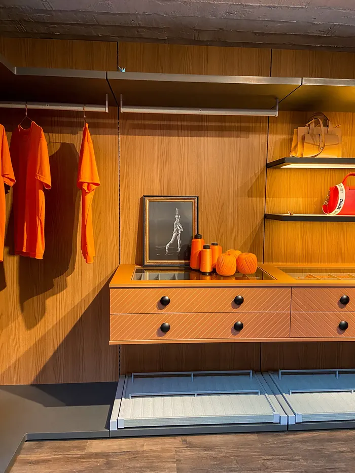 Closet com fundo em madeira, gaveteiro laqueado terracota com ranhuras diagonais e puxadores esféricos pretos.