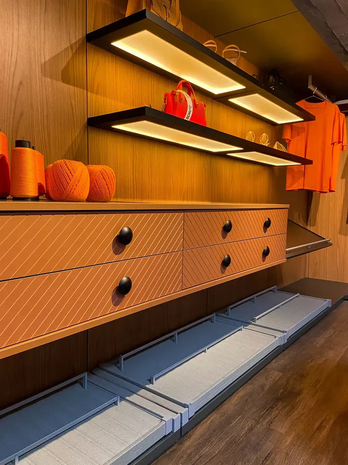 Detalhe de closet com prateleiras iluminadas por perfil de LED e gaveteiro ranhurado terracota.